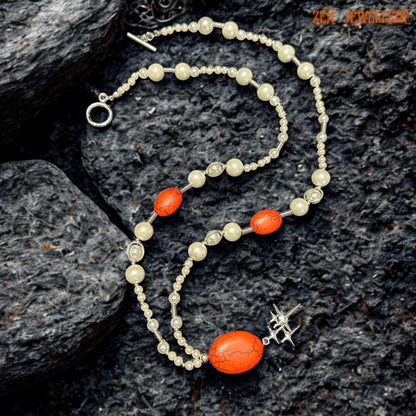 Close-up image of the white pearl necklace with vibrant red coral beads displayed against warm skin tones showing the elegant contrast between soft ivory beads and bold red gemstone details. The necklace features silver spacer accents, symmetrical bead placement, and a polished silver star charm hanging beneath the central coral pendant for a celestial handmade appearance.